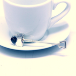 A small silver spoon shaped like a miniature shovel resting on a white ceramic cup and saucer.
